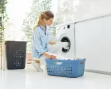 Frau lädt Wäsche in die Waschmaschine. So kann man eine Daunenjacke waschen ohne Trockner.