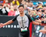 Triathlet Rico feiert seinen Zieleinlauf beim Ironman Luxembourg. Jubelnde Zuschauer reichen ihm die Hände.