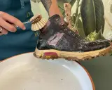 Schuhbürste reinigt schmutzige Wanderschuhe in Seifenwasser. So pflegen Sie Ihre Wanderschuhe richtig.