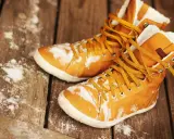 Warme, gefütterte Stiefel mit gelben Schnürsenkeln liegen auf einer Holzplanke, bedeckt mit etwas Schnee. Sie warten darauf, dass die **Schuhe trocknen**.