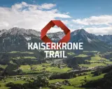 Majestätische Berge über grünen Tälern, mit dem Schriftzug "KAISERKRONE TRAIL" und einem roten Logo.