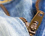 Nahaufnahme eines Reißverschlusses an Jeans. Der Schieber ist halb geöffnet. Ein guter Zeitpunkt, um den Reißverschluss reparieren zu lassen.