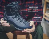 Mann mit kariertem Hemd zeigt, wie man Wanderschuhe bindet. Der Schuh hat zwei Schnürzonen für optimalen Halt.