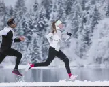 Zwei Läufer in warmer Winterkleidung genießen einen Lauf im Schnee.