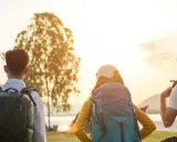Drei Rucksackträger blicken auf den Bodensee. Die Sonne geht unter und taucht die Landschaft in warmes Licht. Eine perfekte Kulisse für eine Wanderung am Bodensee.