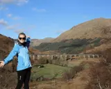 Glückliche Frau genießt das Wandern in Schottland vor einer beeindruckenden Brücke in den Highlands.