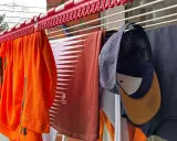 Wäscheleine mit Kleidung, darunter ein orangefarbenes Shirt, ein braunes Shirt und eine Kappe, die zum cap reinigen aufgehängt wurde.