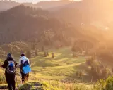 Zwei Wanderer genießen einen **great trail** in Kanada. Die Sonne taucht die bewaldeten Hügel in goldenes Licht.