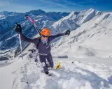 Ein Mann im orangefarbenen Helm jubelt beim Skyrunning in den verschneiten Alpen.