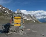 Wegweiser für die Tour du Mont Blanc Etappen: Rucksack und Stöcke liegen bereit. Bergpanorama mit blauen Himmel und Wolken.
