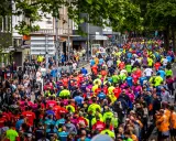 Große Menschenmenge beim Firmenlauf Essen, viele Läufer in bunten Trikots auf einer Straße, umgeben von Bäumen und Gebäuden.