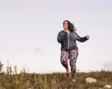 Frau joggt mit Gewichten in bunter Hose durch die Natur.