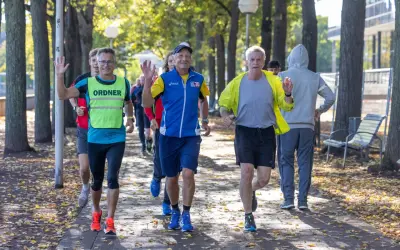 Herren genießen slow jogging im Herbstpark, einige winken fröhlich.
