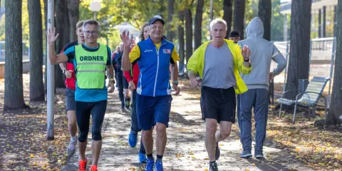 Herren genießen slow jogging im Herbstpark, einige winken fröhlich.