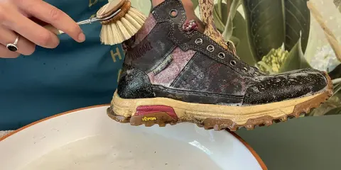 Schuhbürste reinigt schmutzige Wanderschuhe in Seifenwasser. So pflegen Sie Ihre Wanderschuhe richtig.