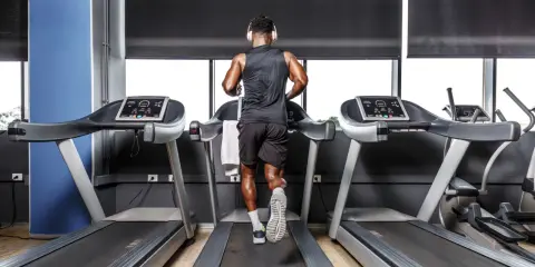 Mann mit Kopfhörern absolviert ein intensives Laufband Training im Fitnessstudio.