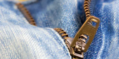 Nahaufnahme eines Reißverschlusses an Jeans. Der Schieber ist halb geöffnet. Ein guter Zeitpunkt, um den Reißverschluss reparieren zu lassen.
