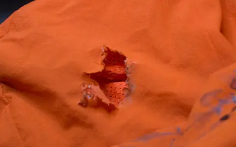 Ein Loch in einer orangefarbenen Polyesterjacke, bereit für einen Flicken.