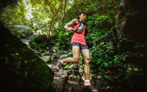 Läuferin bewältigt eine anspruchsvolle ultramarathon distanz auf einem schmalen, steinigen Pfad im dichten Dschungel.