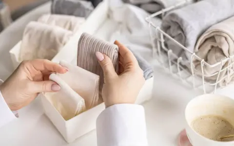 Hände sortieren gefaltete Socken in einer Schubladenteilung. Nach dem Wandersocken waschen ist Ordnung angesagt.