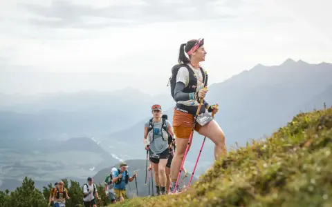 Läuferinnen und Läufer trainieren bergauf gehen in den Alpen. Sie nutzen Stöcke zur Unterstützung.
