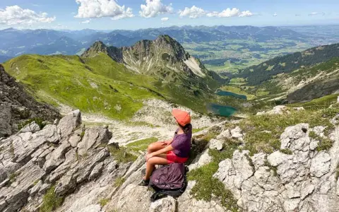 Ein Mädchen mit Rucksack genießt die Aussicht auf die Berge bei Oberstdorf. Ein leichtes Wandern mit toller Belohnung.