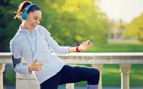 Frau mit Kopfhörern und Handy-Armband spielt Luftgitarre beim Joggen. Die Musik zum Joggen macht sie glücklich.