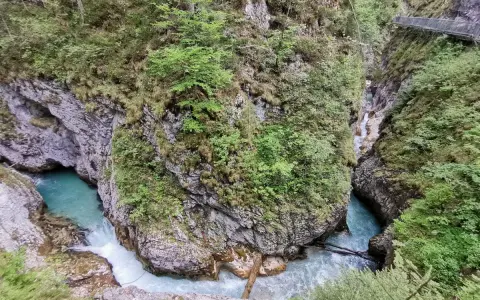 Türkisblaues Wasser rauscht durch eine enge Schlucht mit steilen Felswänden, bewachsen mit üppigem Grün. Eine Holzbrücke führt über die Klammen in Bayern.