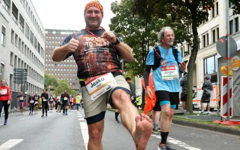 Mann mit schmutzigen Füßen jubelt nach einem Halbmarathon ohne Training. Er hält eine Medaille hoch und gibt Daumen hoch.