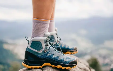 Graue Socken und blaue Wanderschuhe mit gelber Sohle stehen auf einem Felsen. Bereit für das nächste Abenteuer in den Bergen.