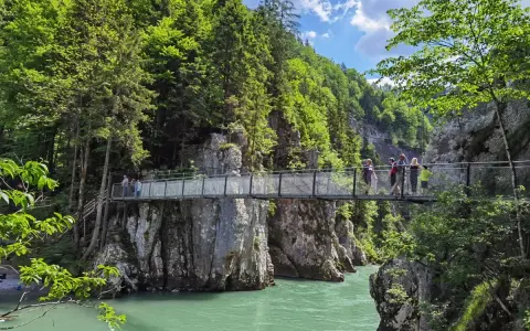 Menschen überqueren eine Hängebrücke während einer entenlochklamm wanderung. Türkises Wasser fließt unter der Brücke hindurch, umgeben von steilen Felswänden und üppigem Grün.