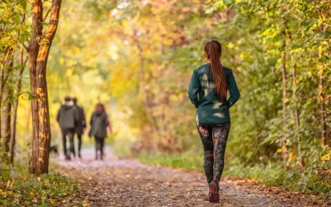 Frau im Herbstwald beim Power Walking, während im Hintergrund ein Paar spazieren geht.