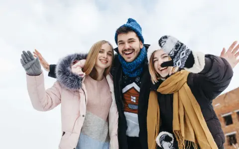 Drei Freunde genießen das Wandern im Winter. Sie tragen warme Kleidung wie Daunenjacken, Mützen und Handschuhe.