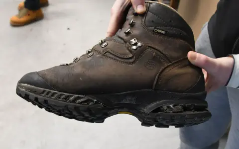 Brauner, abgenutzter Wanderschuh wird gehalten. Die Sohle ist stark abgenutzt, was zeigt, dass die Schuhe besohlen lassen werden müssen, um sie wieder einsatzfähig zu machen.