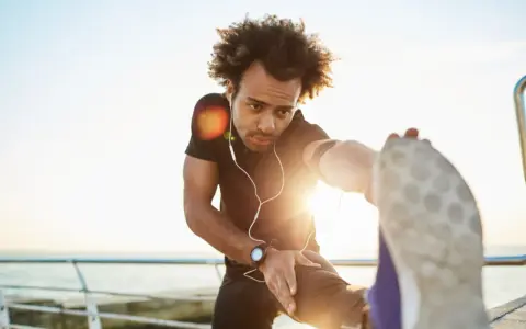 Mann dehnt sich am Meer, wichtig für die Regeneration nach Halbmarathon.