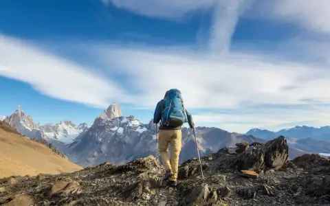 Ein Wanderer mit Rucksack und Stöcken erklimmt einen felsigen Grat. Die majestätische Bergkulisse zeigt die wahre trekking bedeutung: Abenteuer und Freiheit.