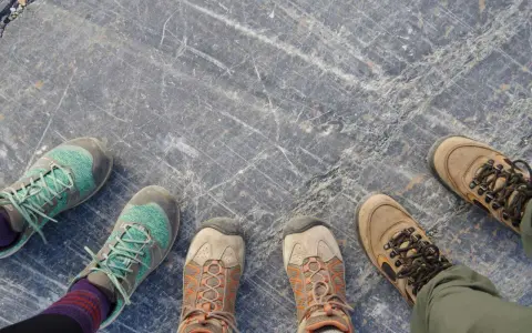 Vier Paar Wanderschuhe auf grauem Steinboden. Sie zeigen, wie sollten Wanderschuhe sitzen: bequem, aber fest.