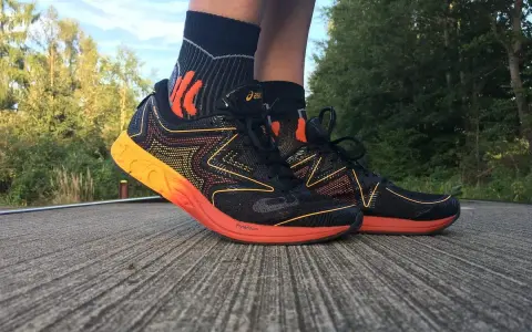 Asics Gel NoosaFast Laufschuhe in Schwarz mit orangen Akzenten, bereit für den nächsten Lauf im Grünen.