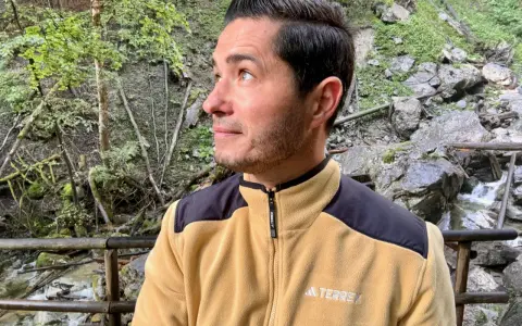 Mann in gelber Fleecejacke mit schwarzem Kragen und Schulterpartien, die zeigt, welche Fleecejacke wirklich warm ist.