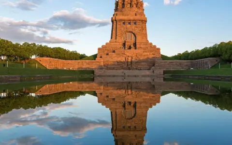 Das Völkerschlachtdenkmal in Leipzig spiegelt sich im Wasser. Ein Läufer genießt die Abendstimmung.