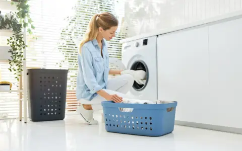 Frau lädt Wäsche in die Waschmaschine. So kann man eine Daunenjacke waschen ohne Trockner.