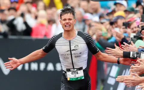 Triathlet Rico feiert seinen Zieleinlauf beim Ironman Luxembourg. Jubelnde Zuschauer reichen ihm die Hände.