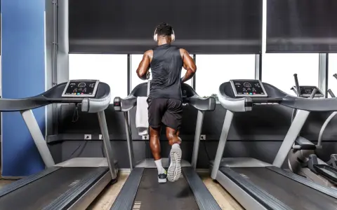 Mann mit Kopfhörern absolviert ein intensives Laufband Training im Fitnessstudio.