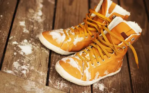 Warme, gefütterte Stiefel mit gelben Schnürsenkeln liegen auf einer Holzplanke, bedeckt mit etwas Schnee. Sie warten darauf, dass die **Schuhe trocknen**.