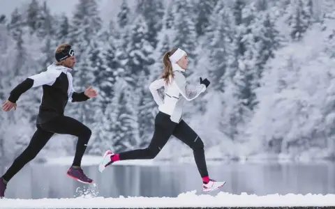 Zwei Läufer in warmer Winterkleidung genießen einen Lauf im Schnee.