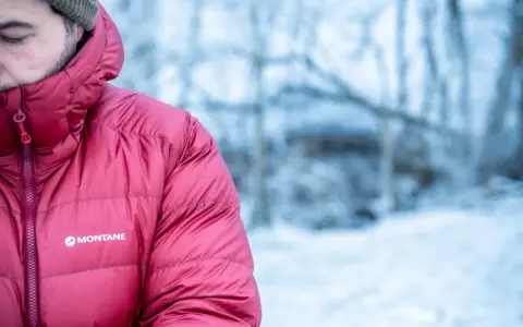 Mann in roter Montane-Jacke mit Kapuze im Schnee. Gute thermore ecodown erfahrungen im Winter.