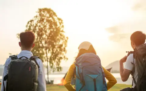 Drei Rucksackträger blicken auf den Bodensee. Die Sonne geht unter und taucht die Landschaft in warmes Licht. Eine perfekte Kulisse für eine Wanderung am Bodensee.