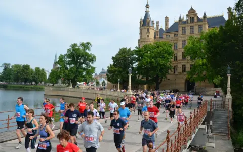 Teilnehmer des 5 Seen Lauf Schwerin überqueren eine Brücke vor dem Schloss.