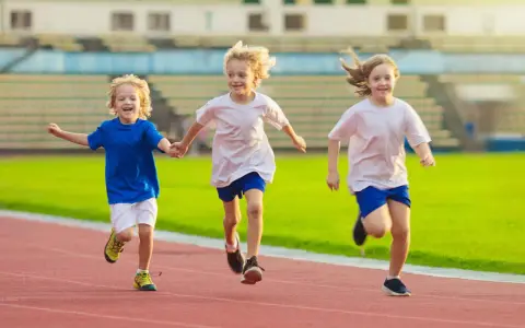 Drei lachende Kinder beim Lauftraining auf einer roten Laufbahn. Sie rennen nebeneinander, die Arme ausgestreckt.