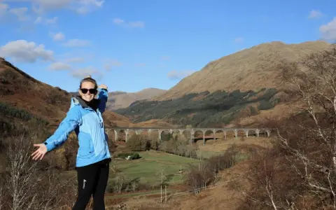 Glückliche Frau genießt das Wandern in Schottland vor einer beeindruckenden Brücke in den Highlands.